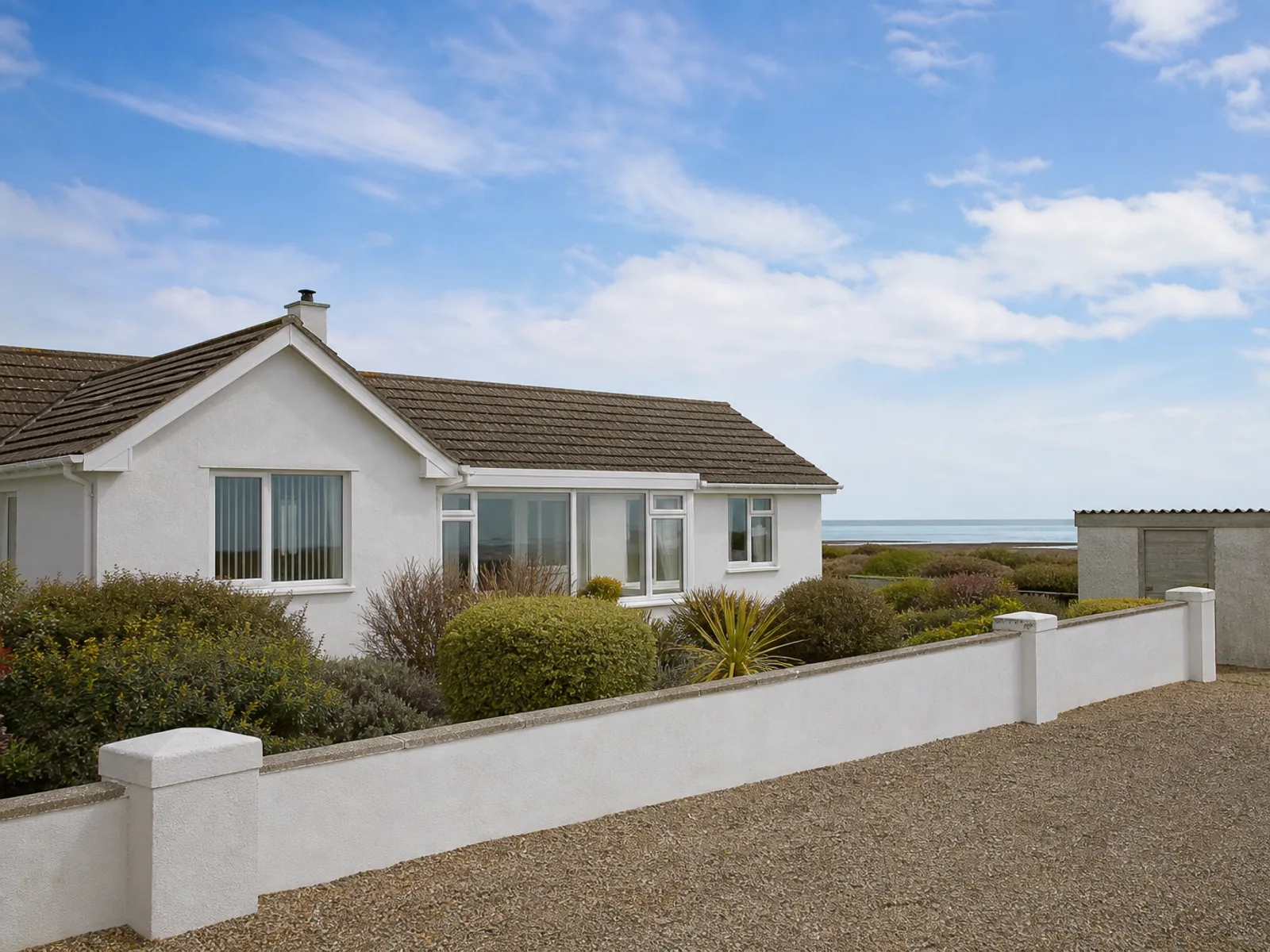 White rendered seaside bungalows with a cement-sheet outbuilding under open sky on Hayling Island